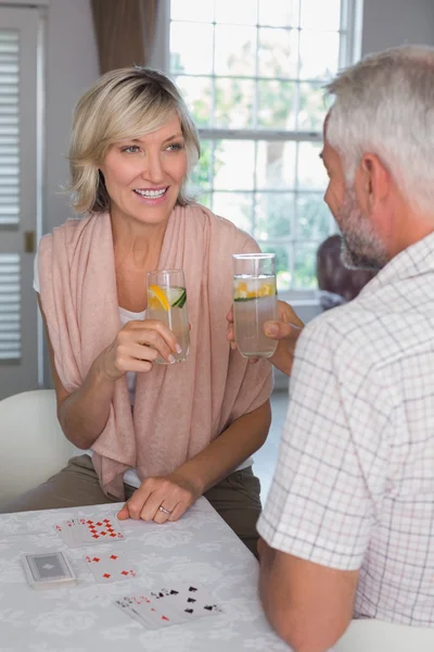 Mature couple toasting drinks while playing cards at home — Stock Photo, Image