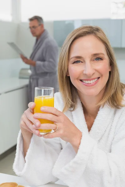 Leende kvinna med apelsinjuice med mannen i bakgrunden — Stockfoto