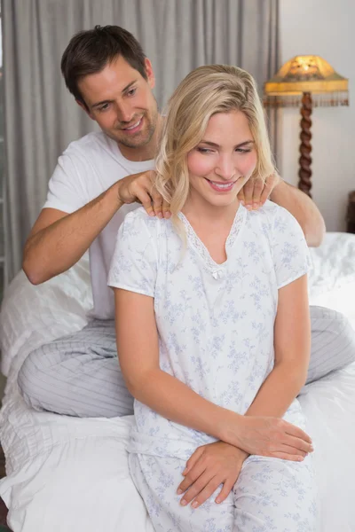 Uomo sorridente massaggiare le spalle della donna a letto — Foto Stock