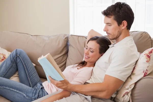 Relajada pareja joven leyendo libro en el sofá — Foto de Stock