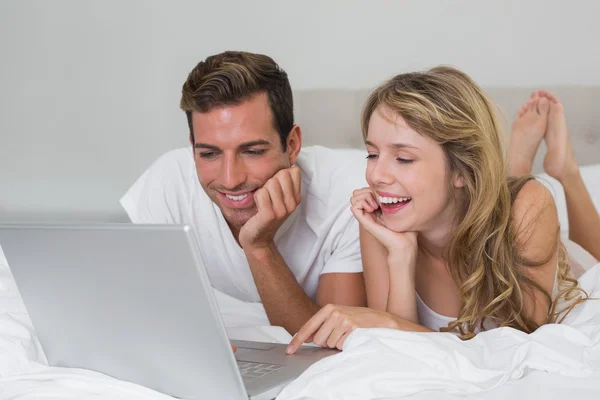 Gelukkige jonge paar met laptop in bed — Stockfoto