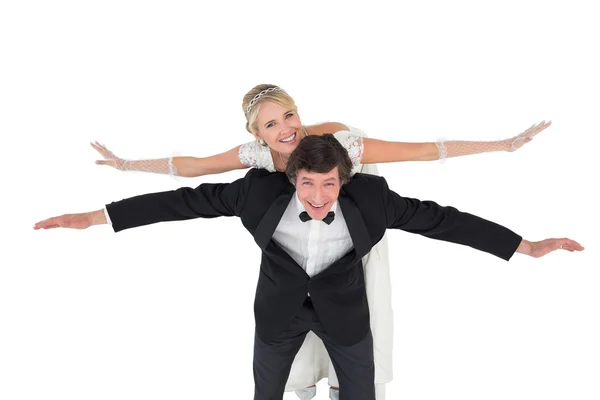 Groom with arms outstretched carrying bride on back — Stock Photo, Image