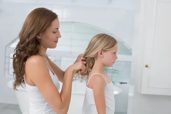 Femme tressant les cheveux de la petite fille mignonne dans la salle de bain — Photo