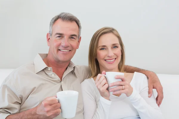 Uvolněné milující pár s šálky s kávou v obývacím pokoji — Stock fotografie