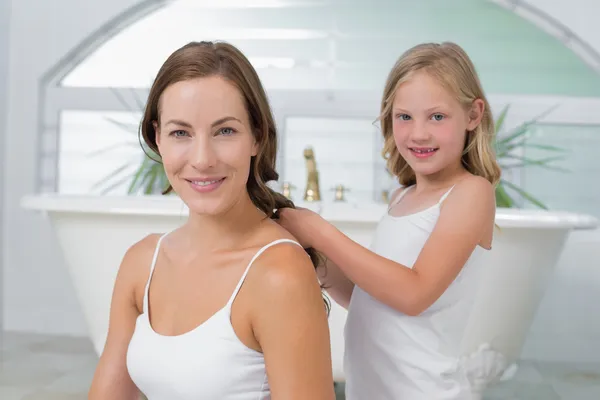 Милая маленькая девочка плетет мамины волосы в ванной — стоковое фото