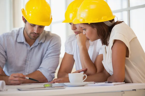 Arquitectos en cascos amarillos trabajando en planos — Foto de Stock