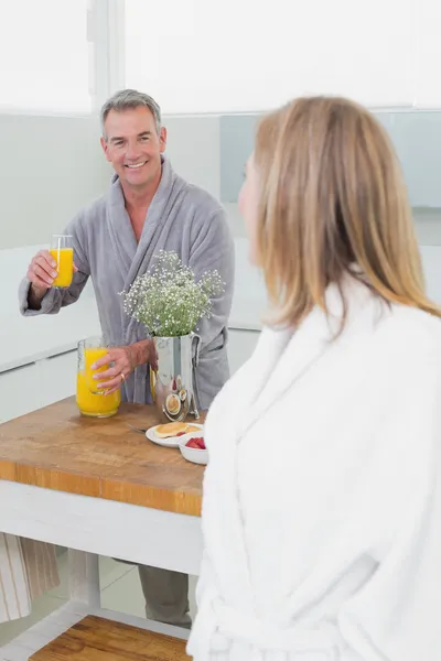 Homem oferecendo suco de laranja para mulher na cozinha — Fotografia de Stock