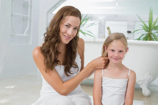 Mujer sonriente trenzando el pelo de la niña linda en el baño —  Fotos de Stock