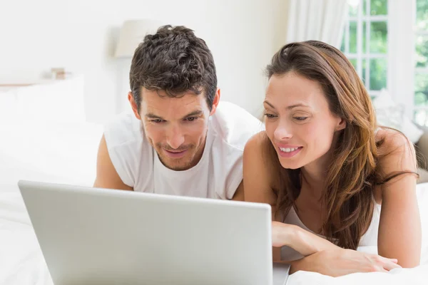 Smiling couple using laptop in bed — Stock Photo, Image