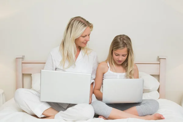 Mor och dotter med bärbara datorer i sängen — Stockfoto