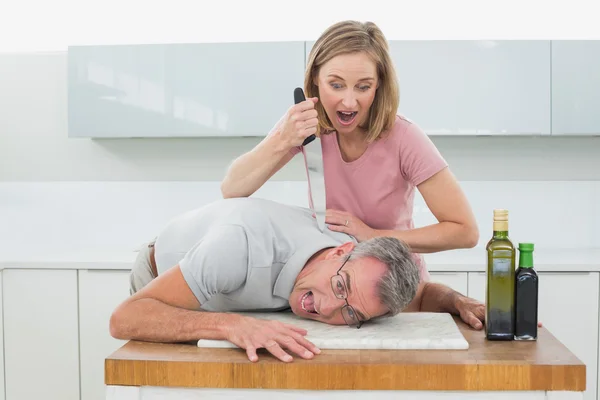 Woman holding knife to man's neck in kitchen — Stock Photo, Image