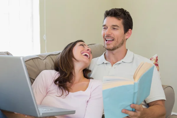 Cheerful couple with laptop and book at home — Stock Photo, Image