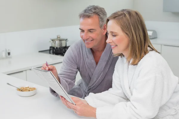 Couple in bathrobes reading newspaper in kitchen — Stock Photo, Image