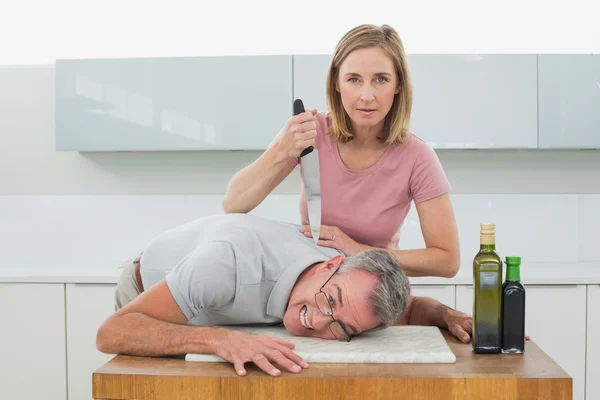 Mujer sosteniendo cuchillo al cuello del hombre en la cocina — Foto de Stock