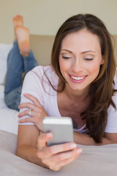 Leende kvinna med mobiltelefon i sängen — Stockfoto