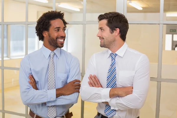Dwóch biznesmenów uśmiechający się z rękami skrzyżowanymi w biurze — Zdjęcie stockowe