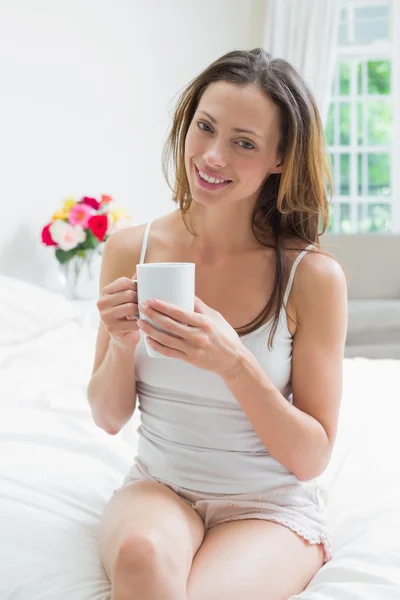 Улыбающаяся расслабленная женщина с чашкой кофе, сидящей в постели — стоковое фото