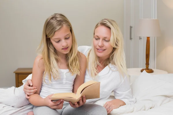 Mor och dotter läser bok i sängen — Stockfoto