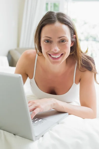 Sonriendo mujer relajada usando el ordenador portátil en la cama —  Fotos de Stock