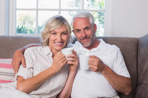 ยิ้มคู่ผู้ใหญ่กับถ้วยกาแฟในห้องนั่งเล่น — ภาพถ่ายสต็อก