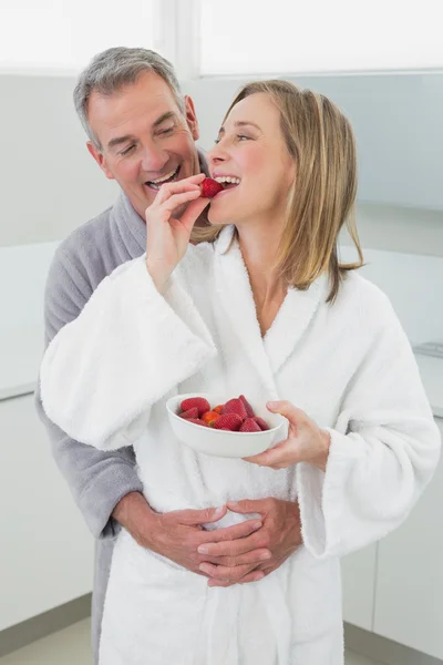 Homem abraçando mulher como ela come morango na cozinha — Fotografia de Stock