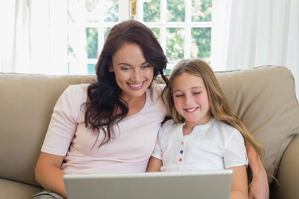 Мать и дочь используют ноутбук вместе на диване — стоковое фото
