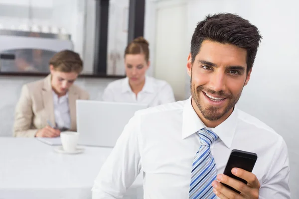 Businessman text messaging with colleagues at office desk — Stock Photo, Image