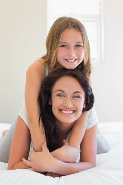 Girl sitting on mother in bedroom — Stock Photo, Image
