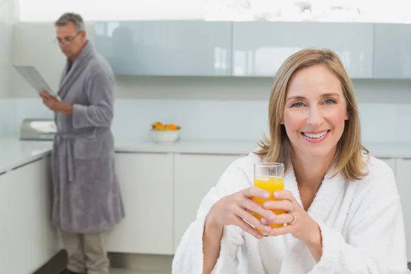 Улыбающаяся женщина держит апельсиновый сок с мужчиной на заднем плане — стоковое фото