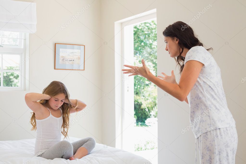 Girl covering ears while mother scolding bedroom