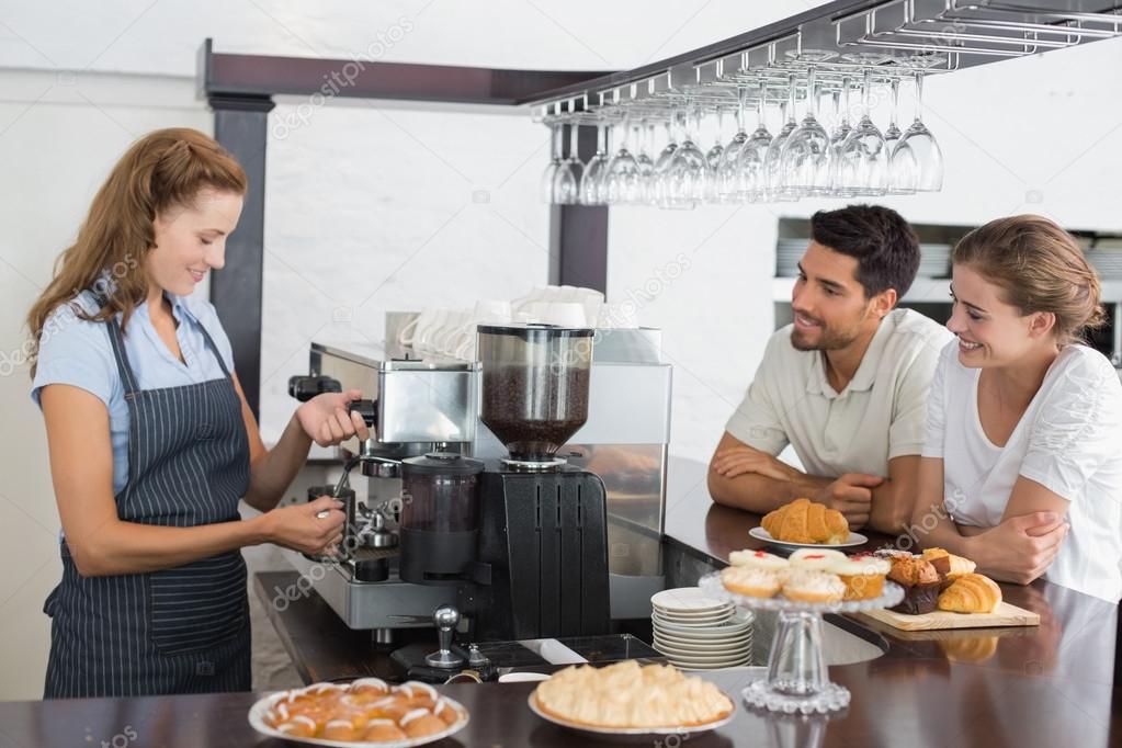 Couple looking at waitress prepare coffee at coffee shop