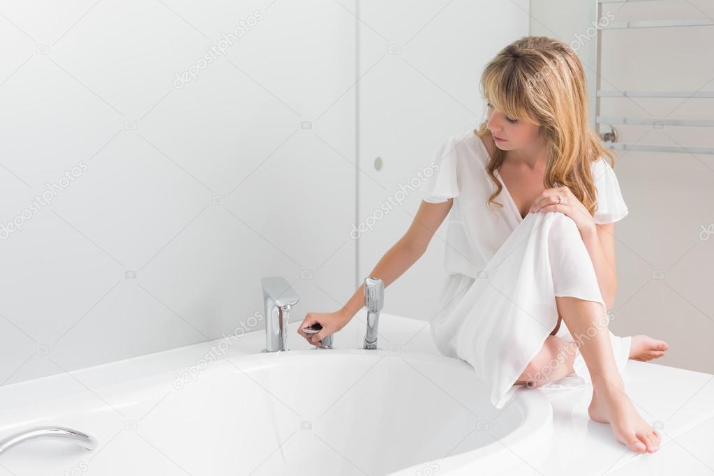 Beautiful young woman sitting on the edge of bath tub