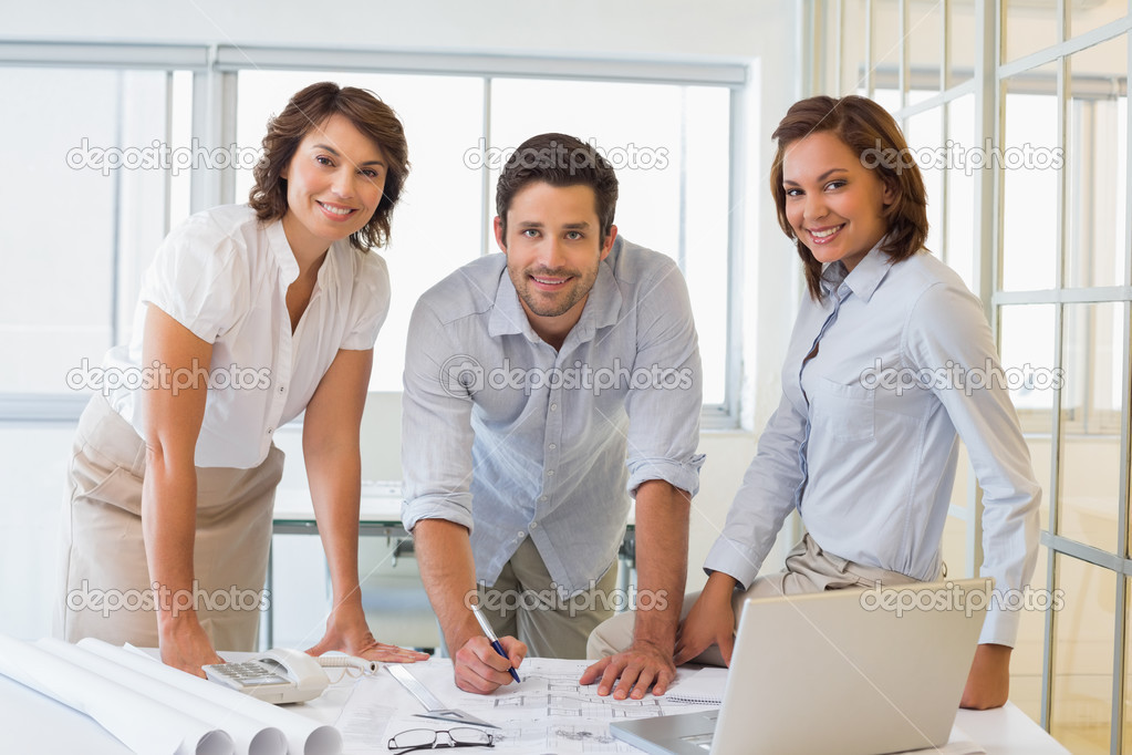 Smiling business people working on blueprints at office