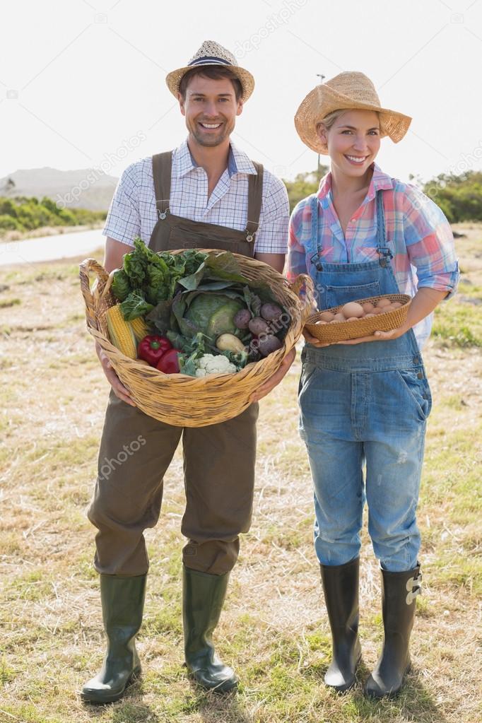 Smiling couple with vegetables standing in field