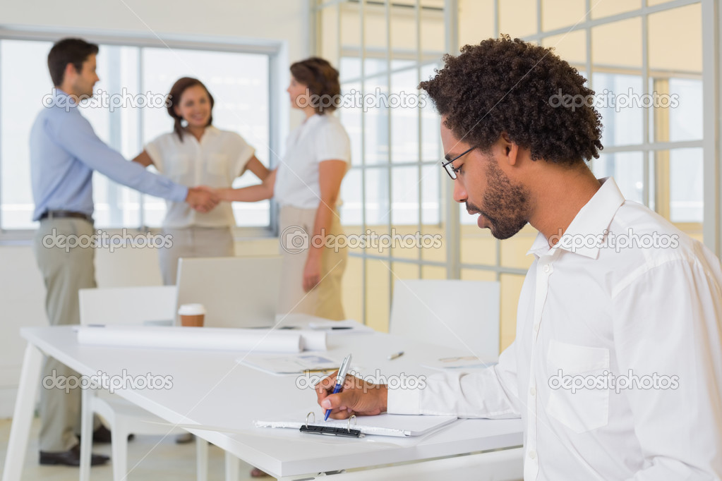 Businessman writing notes with colleagues shaking hands in office