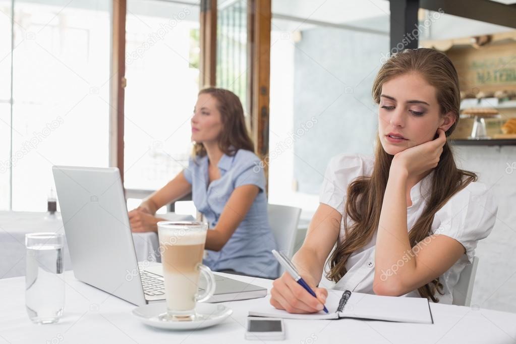Woman writing notes with laptop in coffee shop