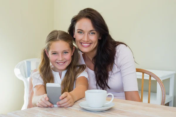 Woman and daughter holding mobile phone at table — Stock Photo, Image