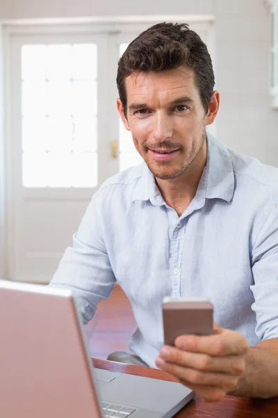 Smiling young man using laptop and mobile phone — Stock Photo, Image