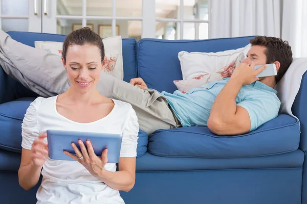 Пара с помощью цифрового планшета и мобильного телефона в гостиной — стоковое фото