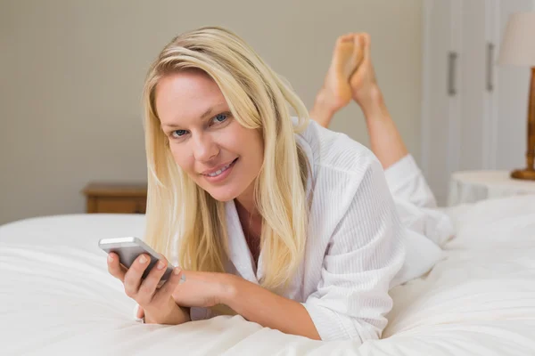 Γυναίκα, κρατώντας το κινητό τηλέφωνο ενώ ξαπλωμένη στο κρεβάτι — Φωτογραφία Αρχείου