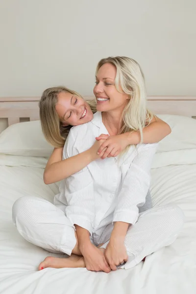 Menina abraçando a mãe sentada na cama — Fotografia de Stock