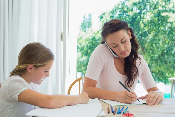 Vrouw met behulp van mobiele telefoon terwijl dochter studeren aan tafel — Stockfoto