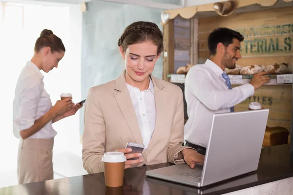 Zakenvrouw met behulp van mobiele telefoon en laptop in office cafetaria — Stockfoto