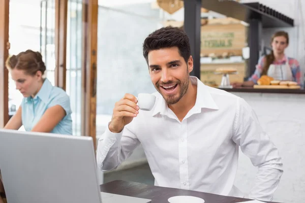 Homme joyeux boire du café tout en utilisant un ordinateur portable dans un café — Photo