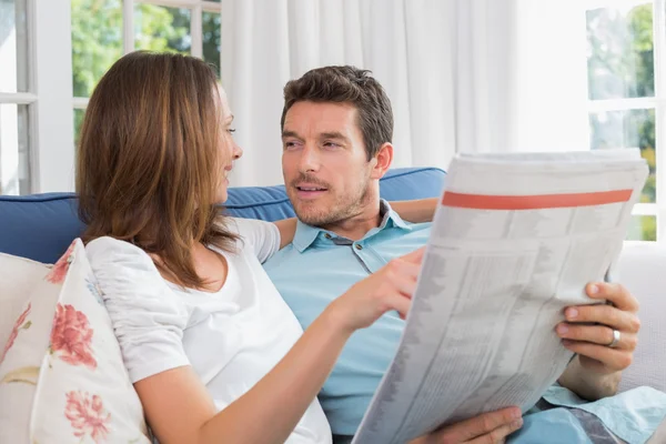 Relajada pareja feliz leyendo el periódico en el sofá —  Fotos de Stock