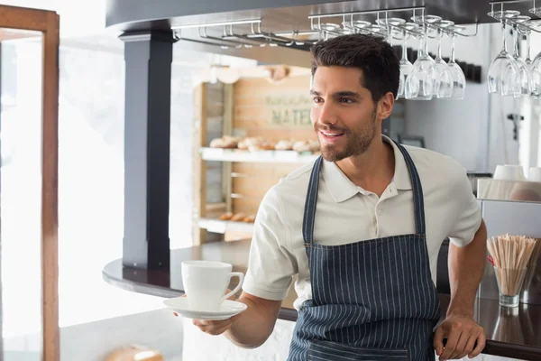 Camarero sonriente sosteniendo taza de café en la cafetería — Foto de Stock