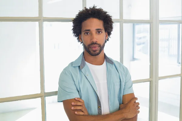 Serious casual young businessman with arms crossed in office — Stock Photo, Image