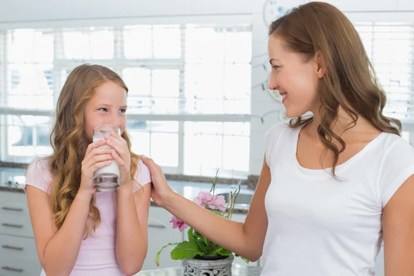 Girl drinking milk as she looks to her mother in kitchen — Stock Photo, Image