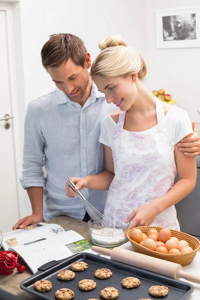 Couple looking at cook book and preparing cookies in kitchen — Stock Photo, Image