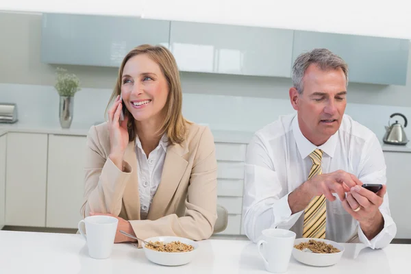 Business par använda mobiltelefoner med frukost i köket — Stockfoto